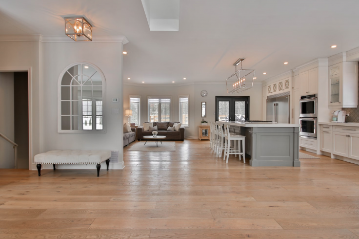 a chic, open plan kitchen living area with white walls, grey units and light wood coloured luxury tiles.